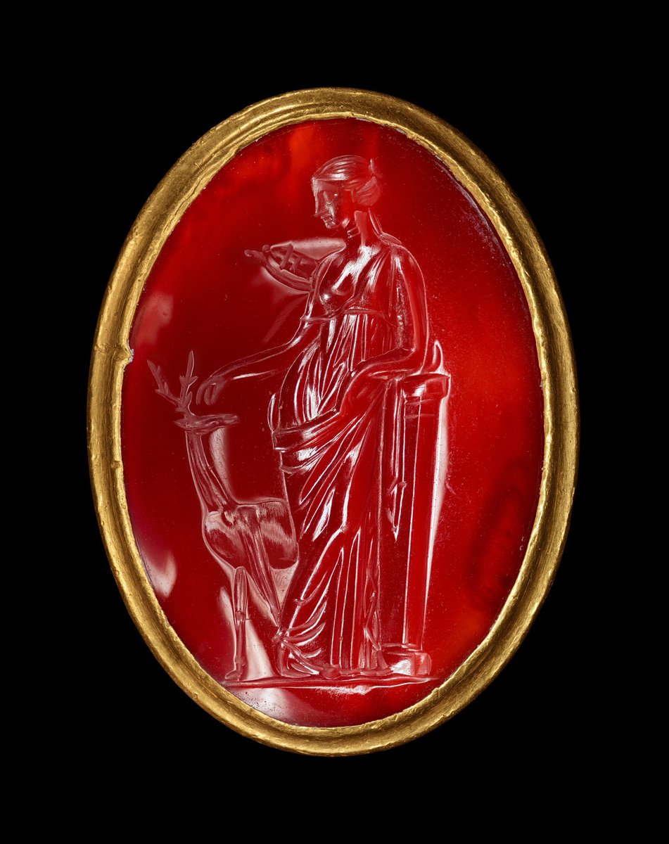 This delightful Egyptian (c. 225 BCE - Ptolemaic Period) gold ring inset with an intaglio depicts the Greek goddess Artemis. Carved on a cabochon carnelian, she leans on a pillar and reaches to pet the head of a stag. 🏛️@GettyMuseum #Classics #Greek #Egypt #Art #Archaeology