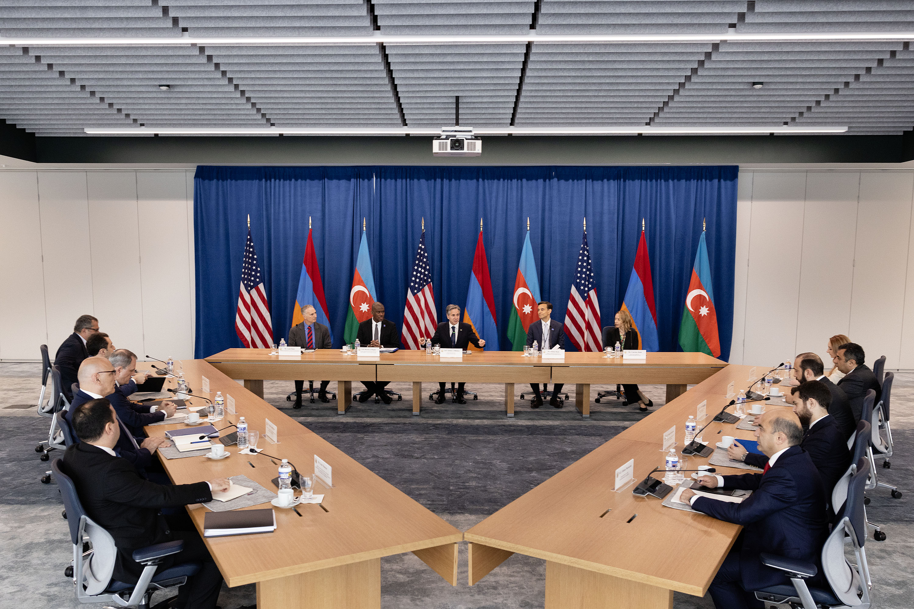 Secretary Blinken sits at a table with U.S. government officials. Foreign Minister Ararat Mirzoyan and Foreign Minister Jeyhun Bayramov sit at two other tables with their officials that form a triangle with the first. U.S., Armenian, and Azerbaijani flags are behind the Secretary. 