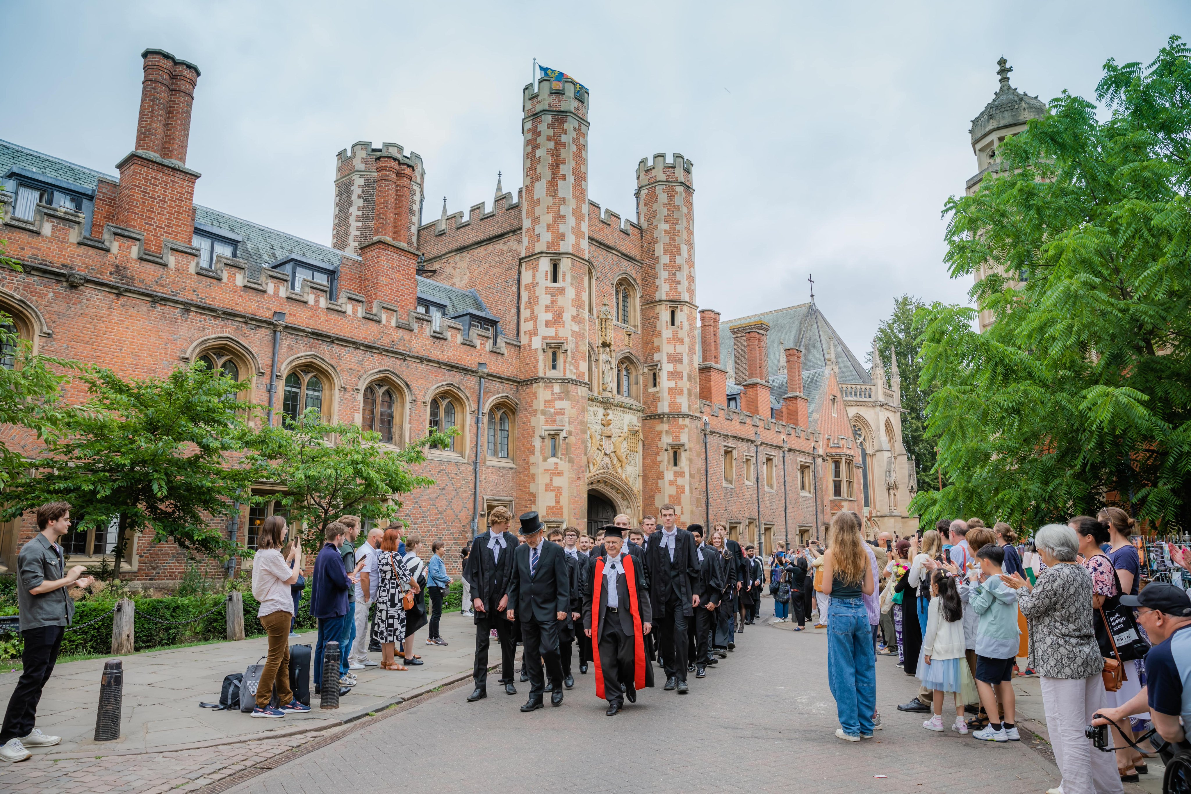 Street-view of St John's College. A parade of graduands led by the Master in formal robes coming towards to the camera.