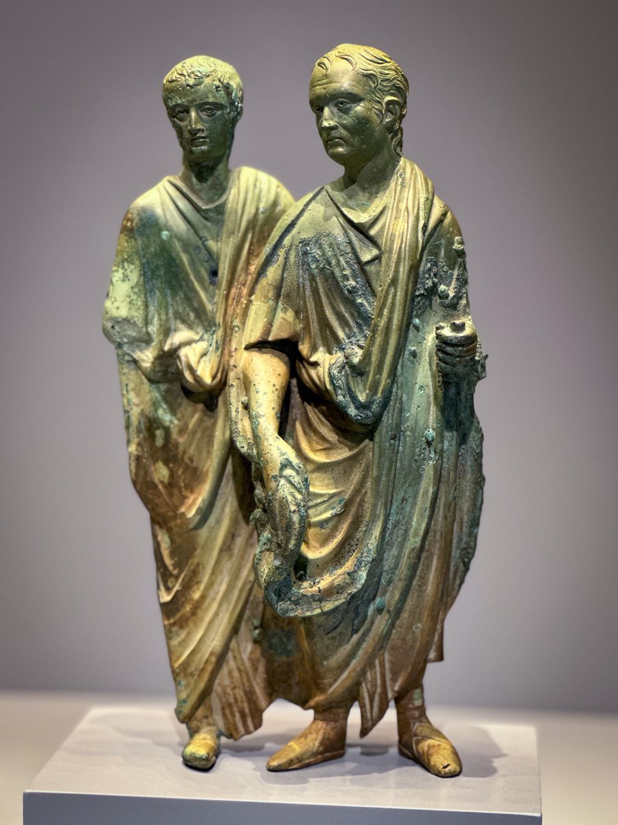 For #ReliefWednesday, a 1st c. CE bronze fragment of a relief, depicting two upper-class Roman men wearing togas. The older man carries a scroll and wears the shoes of a senator, marking him as a magistrate (chief priest). The younger man wears the shoes of an eques (knight).  1/