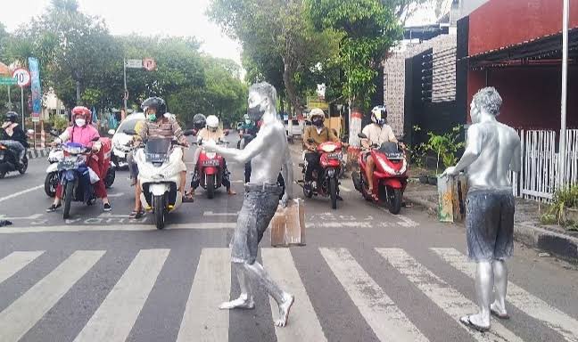 hasyimmah's tweet photo. MANUSIA SILVER

Saya pertama lihat manusia emas/silver itu di trotoar di Kota Bangkok, Thailand sekian tahun yang lalu. Dan dalam setahun terakhir ini saya melihat manusia silver sudah "sampai" di Kota Mojokerto.

Tapi menurut saya, "konsep" manusia silver di Indonesia (konteksnya, yang saya lihat di Mojokerto ya), itu salah. Dan dari kesalahan itu, celakanya malah menyulitkan orang itu sendiri.

Beberapa alasan yang menjadikannya kurang pas dari manusia emas/silver di Indonesia adalah:

Pertama: Konsep awal manusia emas/silver adalah berkamuflase menjadi: PATUNG.

Yang dikerjakan adalah duduk atau berdiri di trotoar dan berharap ada yang memberi uang saat ada yang mengajak foto bareng.

Faktanya di Indonesia (Mojokerto khususnya), mereka bawa kaleng dan minta uang di mobil-mobil yang berhenti di lampu merah (lampu lalin).

Kedua: Sebagai patung, manusia emas/silver itu BERPAKAIAN LENGKAP, termasuk topi dan sepatu, plus ada yang berkaca mata.

Dengan berpakaian lengkap, bagian tubuh manusia emas/silver yang harus terkena cat, tentunya lebih sedikit. Bisa dibilang, bagian tubuh yang kena cat hanyalah: muka, sedikit rambut bagian bepakang (karena pakai topi), dan pergelangan tangan hingga jari. Selebihnya, yang dicat adalah: PAKAIANNYA.

Faktanya di Indonesia (Mojokerto khususnya), mereka tak bertopi, tak berkaca mata, bertelanjang dada, bercelana pendek, dan tanpa alas kaki. Praktis, mereka hanya bercelana pendek.

Dengan hanya bercelana pendek, otomatis hampir seluruh tubuhnya harus terkena cat. Menyulitkan dirinya sendiri? Jelas!

Apalagi kalau kita bicara "jam kerja" mereka yang seringnya siang hari di bawah terik matahari. Apakah itu tidak menyiksa diri sendiri?

Terlebih lagi jika (maaf) dia beragama Islam, itu salatnya bagaimana???

Ketiga: Manusia emas/silver adalah sebuah kegiatan yang mengandung unsur seni. Menurut saya ya. 

Namun faktanya di negara kita, manusia silver/emas sama sekali tak ada seninya. Misal ada orang memberi uang, pastinya lebih karena kasihan, bukan karena kagum, apalagi ingin berfoto bersama.

Dari 3 foto yang saya sertakan, kita bisa menilai mana yang lebih sengsara dalam melakukan "pekerjaan"-nya.

Keterangan foto (hasil googling):
- Foto 1 dan 2: manusia silver di Mojokerto 
- Foto 3: manusia emas di Hollywood street.