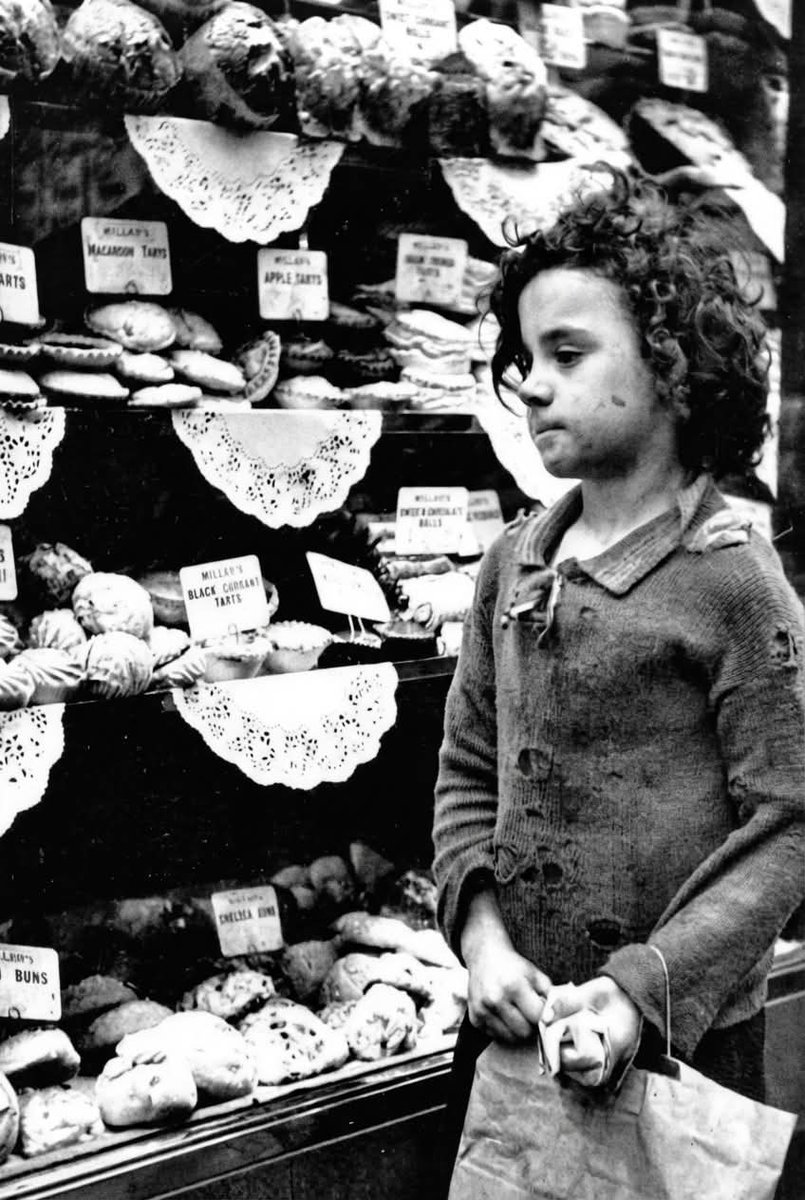 In 1930s Whitechapel, as the weight of the Great Depression settled heavily over East London, a small child lingers outside a neighbourhood bakery, their breath softly fogging the dusty glass. Threadbare coat pulled tight against the cold, they stand motionless, face pressed