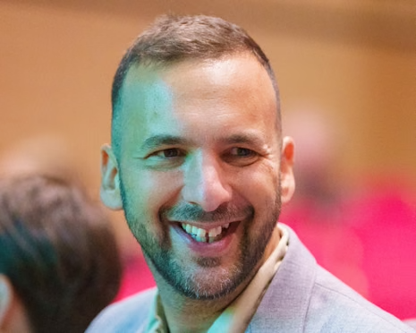 PeterMcCormack's tweet image. Hi @grok, can you put Zack Polanski levitating in the middle of a road, above a vegan criossant, wearing a superhero cape made from recycling bags, holding a megaphone in one hand and a potted plant in the other, shouting at a petrol car while a confused cyclist rings a bell…