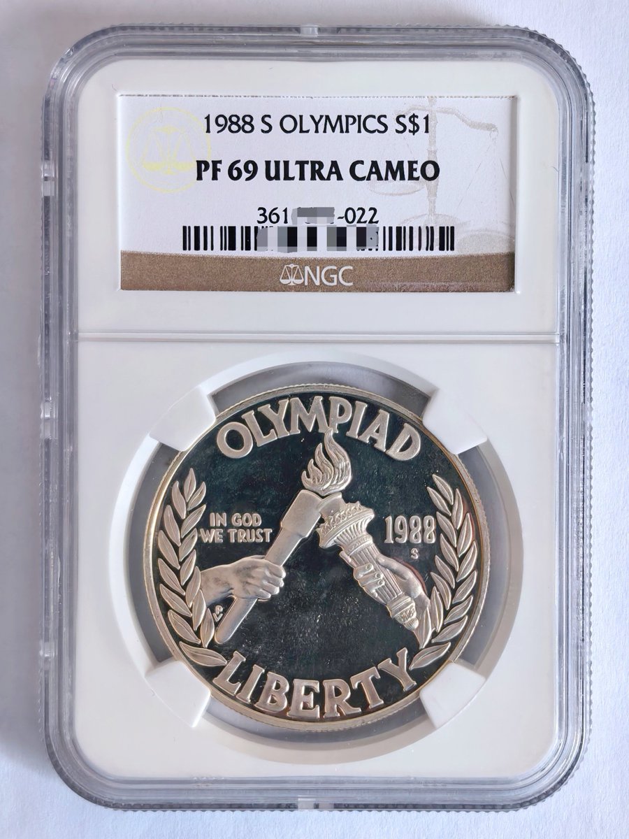 美国1988年“汉城奥运会”纪念银币，正面为手举着的火炬以及自由女神像的火炬，背面为美国奥运队标志。1990年世界硬币 大奖最受欢迎币，重量26.73克，成色为900银，旧金山造币厂铸造的精制版最终发行量1359366枚，NGC评级PF69分。