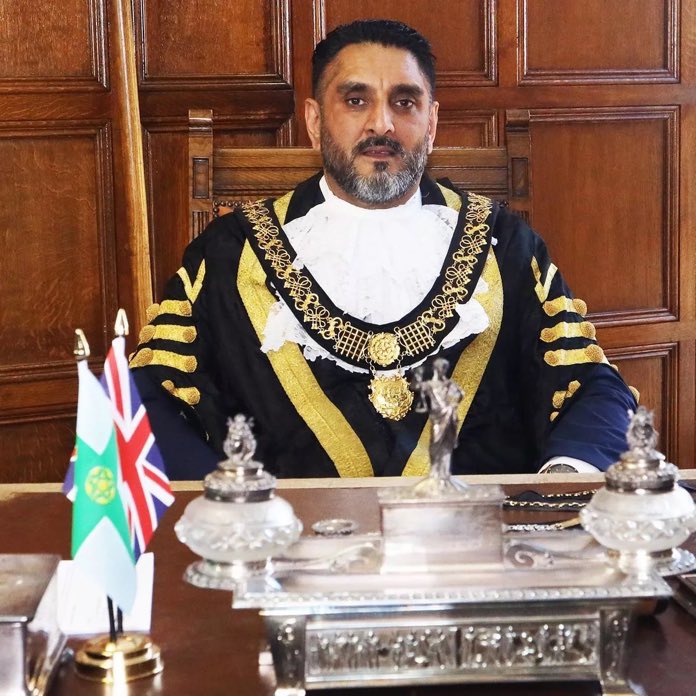 peterstopcrime's tweet image. This is the Mayor of Derby, He is holding an AK47 rifle in front of a portrait of a terrorist called Bhagat Singh, who assassinated a British police officer named John Saunders and then bombed the Central Assembly in Delhi