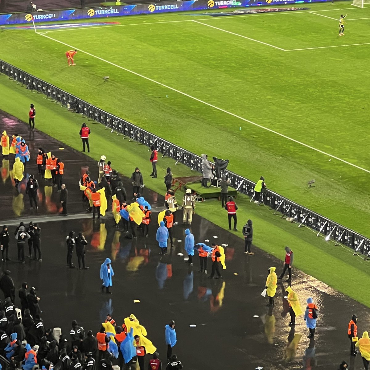 Fenerbahçe taraftarı saha kenarında yağmurdan etkilenen güvenliklere yağmurluklarını attı. Tüm güvenlikler yağmurlukları giyiyor.