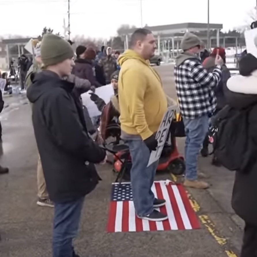 EndWokeness's tweet image. Here's another angle. He's still there, and is stepping on an American flag.