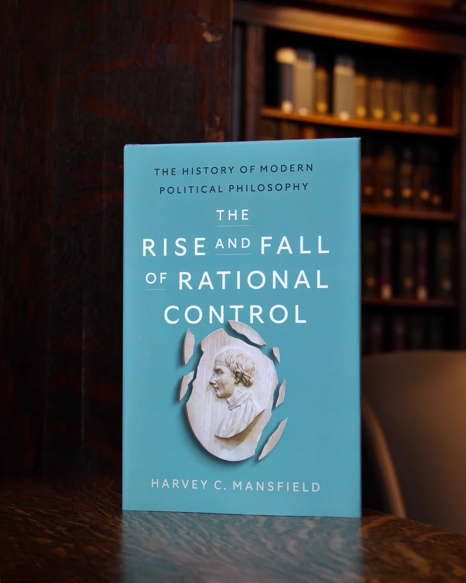 A photo of Harvey C. Mansfield's newest book, The Rise and Fall of Rational Control. On the cover, a shattered medallion of Niccolo Machiavelli. In the background, a blurry bookshelf within Widener Library at Harvard University. The mood is dark and academic.