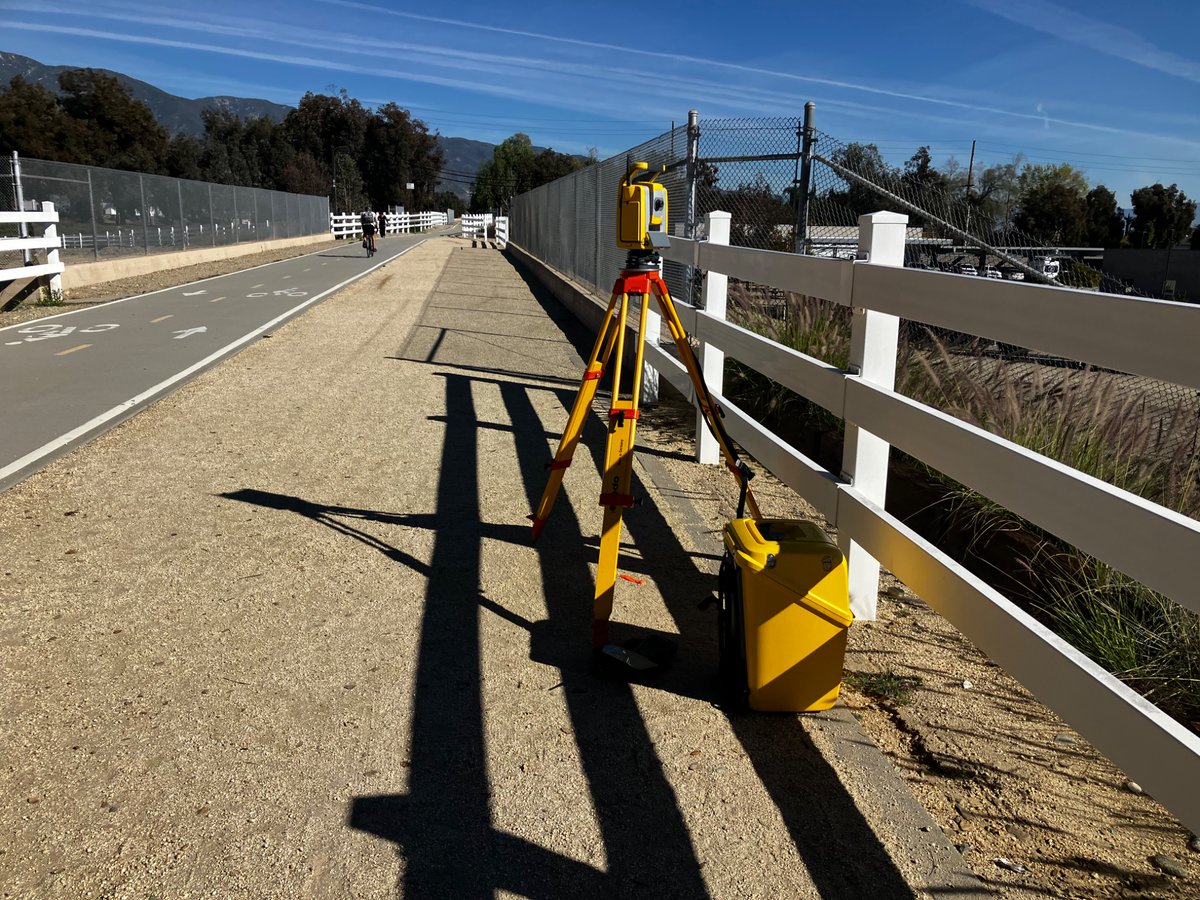 A pair of surveyors, one on the trail and one climbing through the vacant lot are up to something.