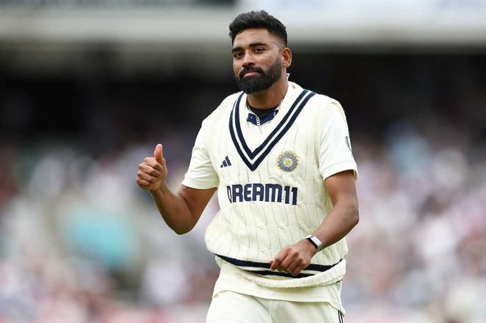 Mohammed Siraj wearing a white cricket jersey with navy blue accents and the BCCI emblem. He has a beard and short dark hair, giving a thumbs-up gesture. The jersey displays "DREAM11" and Adidas logos.