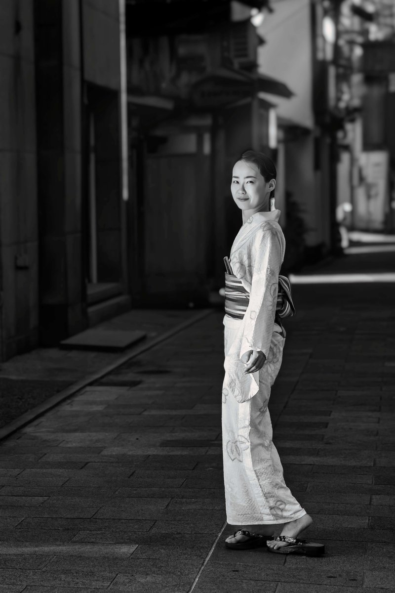 今回は、モノクロで表現してみました。モデルさんの着物に逆光で光が当たっているのが綺麗でこれを表現したかったです。モデルさんの髪の毛が背景の明るい部分に位置していたら良かったなと思いました。飲み屋さんが集まっている裏路地で撮影しました。