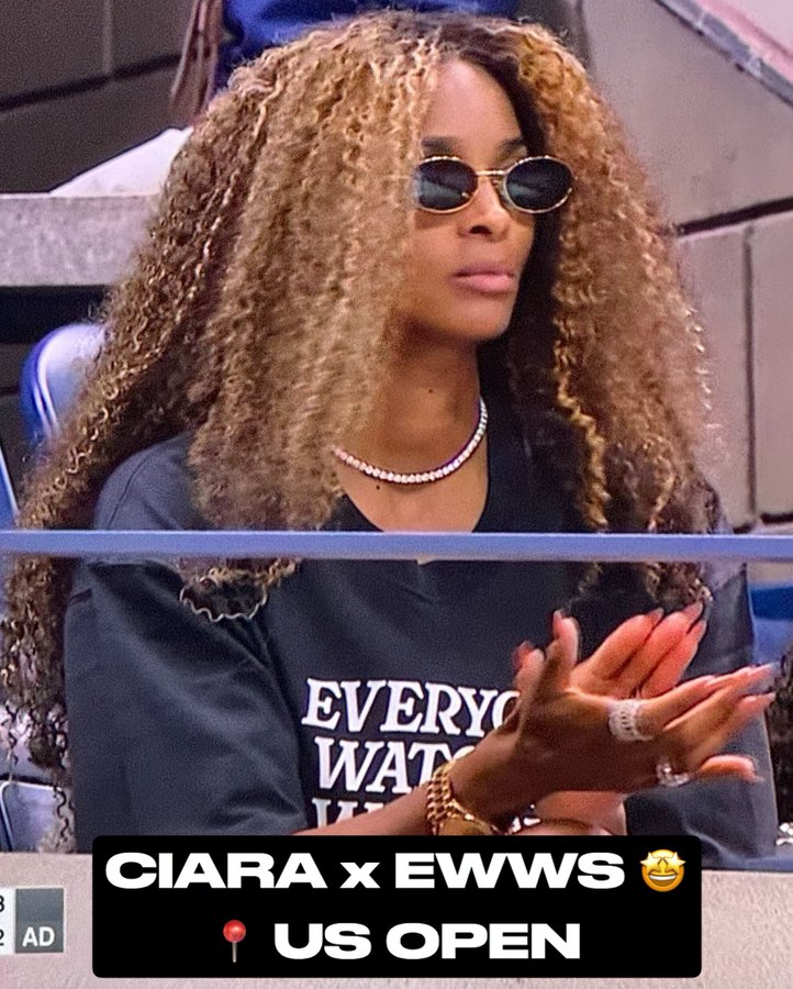 Ciara with long, curly brown hair, wearing sunglasses and a pearl necklace. She is dressed in a dark shirt with "EVERYONE WATCHES WOMENS SPORTS" text. Her hands are visible, adorned with rings and bracelets, clapping. A watermark reading "CIARA x EWWS 😊 US OPEN" is present.