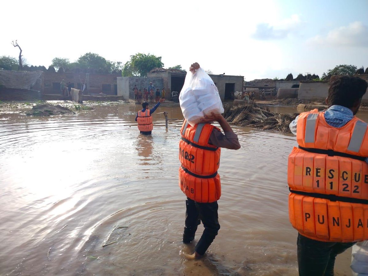 Workers delivering cooked food, ration, and water bottles to inundated homes. Okara.