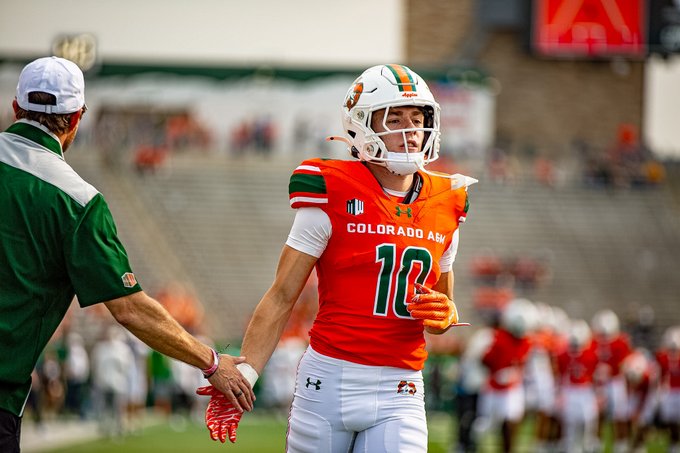 Players wearing orange and green Colorado State football uniforms with helmets featuring a ram logo. One player has the number 10 on the jersey, another has 81, and another has 82. The uniforms display "Colorado State" text and include white pants and gloves. The setting is a stadium with a grassy field and spectators in the background.