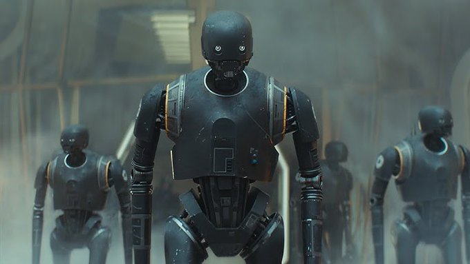 Multiple black droid robots with orange accents standing in a misty, industrial setting. A futuristic spacecraft with a glowing central core and triangular wings in a debris-filled area. A large, circular domed structure in an open plaza with people walking, surrounded by futuristic architecture and mountains. A sleek, futuristic walkway with people in robes crossing a bridge, with a domed building and city skyline in the background.