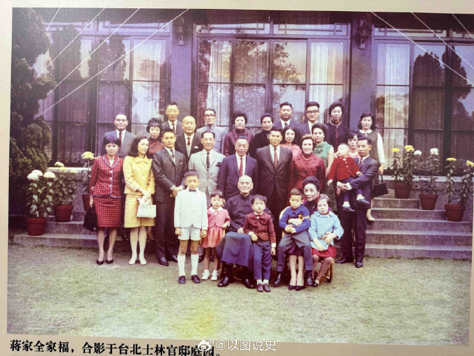一大群人在户外一栋有大窗户和盆栽的建筑前合影留念。蒋介石站在大人和孩子中间，有的穿着西装和连衣裙等正装，有的则穿着休闲装。这群人排成一排，有的坐在台阶上，有的站在草地上。