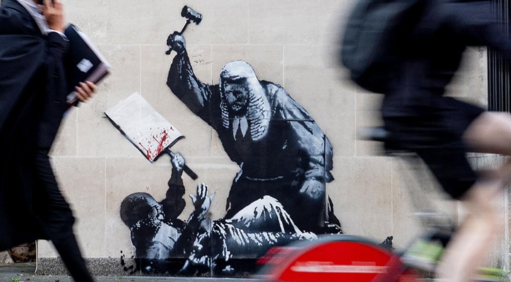 AJEnglish's tweet image. British street artist Banksy has painted a mural outside London's Royal Courts of Justice depicting a judge beating a protester, with reports suggesting it's in response to the arrest of hundreds of demonstrators supporting banned group Palestine Action.

📸: Banksy/Reuters