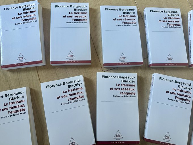 Multiple white books with red and black text, arranged on a wooden surface. The covers display the name "Florence Bergeaud-Blackler" and titles including "Le Frérisme et ses réseaux," "Le Blackler et ses réseaux," and "Le Frérisme et ses réseaux, Professeure d'histoire." A logo with a triangular design is visible on each book.