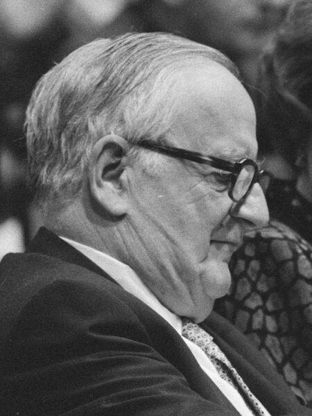 Černobílá fotografie Alexandra Kinga, staršího muže se světlými vlasy, brýlemi a oblekem s kravatou, pohled z profilu ze strany.