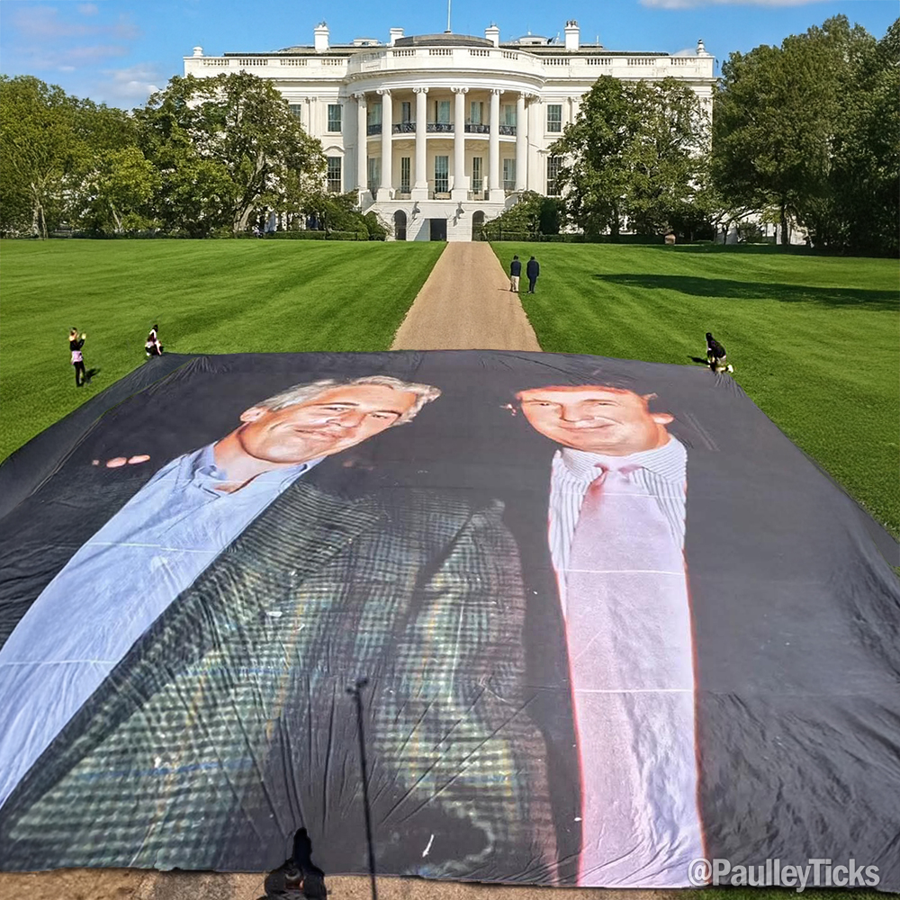 A large banner on the White House lawn displaying two images of Donald Trump in suits and ties. The White House, a white building with columns, is visible in the background with a pathway and green lawn. Several people are scattered on the lawn near the banner.