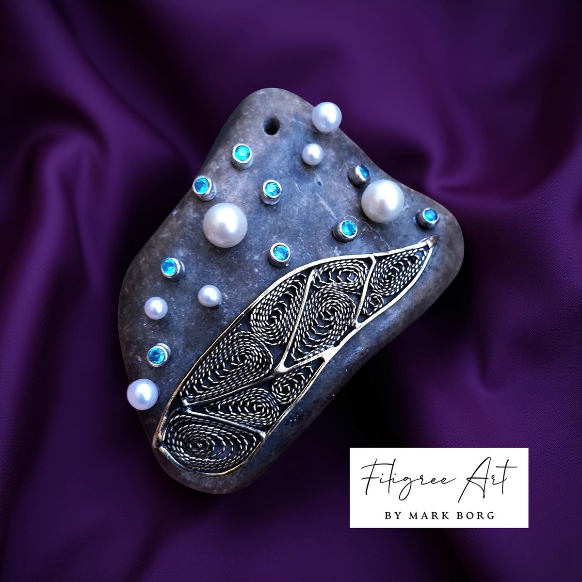 A simple pebble, once forgotten on the shore, now reborn as a vessel of light.
Pearls whisper of the sea’s timeless grace.
Blue stones echo fragments of the heavens.
And across its surface, filigree veins weave a story — delicate, intricate, eternal.
#markborg #filigreart #malta