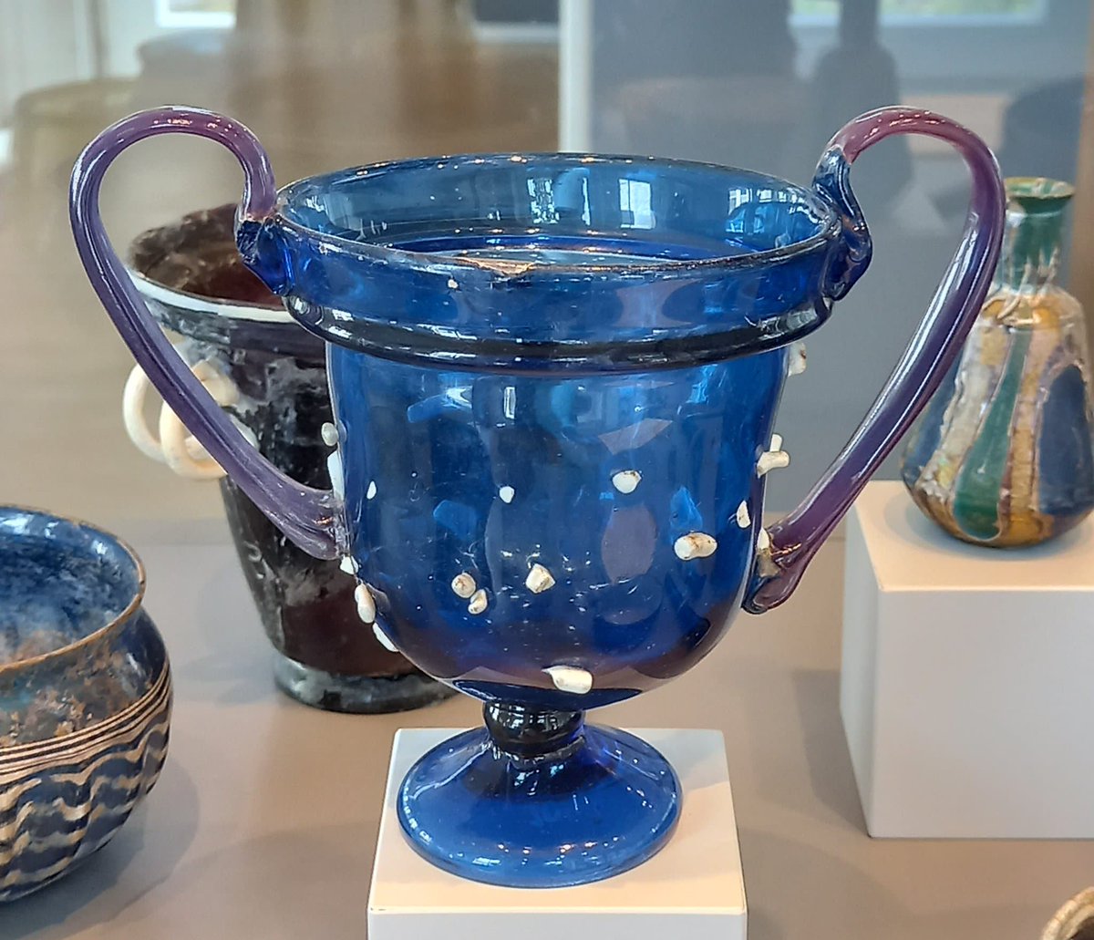 A #Roman two-handled glass cup, in a beautiful cobalt blue with white chips on the outside for extra decoration. Those Romans really knew a thing or two about glassware!