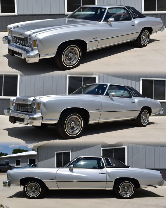 A silver 1975 Chevrolet Monte Carlo car. The vehicle has a sleek design with a two-door coupe body, chrome accents, and whitewall tires. The car is parked on a concrete surface in front of a gray building with windows.