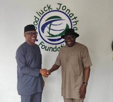 Peter Obi and Goodluck Jonathan shaking hands, both wearing traditional Nigerian attire. Peter Obi is in a gray outfit with a black cap, and Goodluck Jonathan is in a beige outfit with a black hat. A logo behind them reads "Goodluck Jonathan Foundation" with text and a circular design.