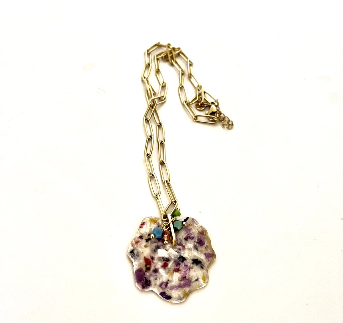 Colgante en acero dorado con efecto escarchado, acompañado de una cadena de eslabones dorados. La pieza se realza con tres cristales tallados que aportan luz y brillo sutil.