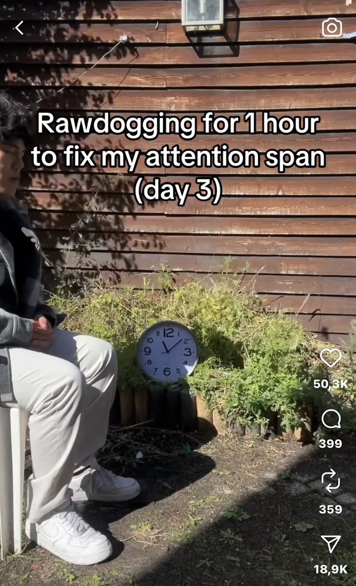 A person sitting outdoors on a bench, wearing light-colored pants and white sneakers. A clock on the ground shows the time, and greenery is visible nearby. A wooden wall with a lantern is in the background. TikTok watermarks are present.