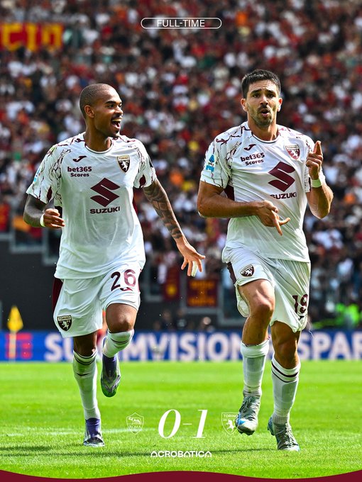 Two soccer players in white jerseys with maroon accents and the Torino FC logo, including Suzuki and Bet365 sponsorships, running on a grass field. One player, wearing jersey number 26, has a bald head and tattoos on his arms. The other, wearing jersey number 16, has dark hair and is pointing with his right hand. The background shows a stadium with a crowd and advertising boards. Text overlays read "FULLTIME" at the top and "0 1" with "OCROBATICA" at the bottom.