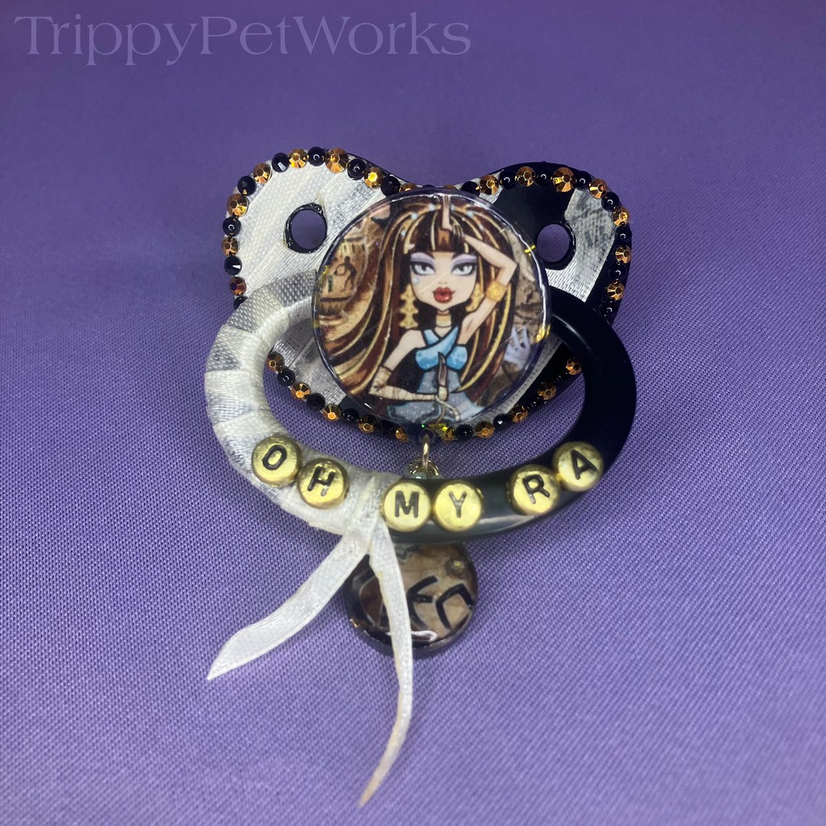TrippyPetWorks's tweet photo. Cleo’s pacifier features a Completely Handmade resin centerpiece and dangle charm! A unique black and gold Rhinestone/ faux pearl design with character personality in mind! Bandages (ribbon) And the nipple filled with gold flakes! Always durable for worry-Free Use!˚𝜗𝜚˚⋆ https://t.co/hRvlWirSjH
