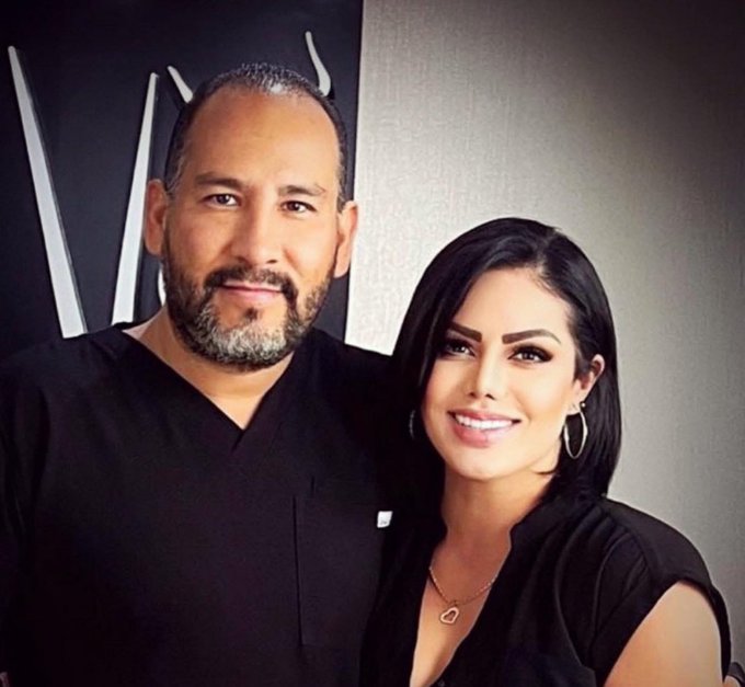 Paloma 'N' and Víctor 'N' standing together, both wearing dark clothing. Paloma 'N' has short dark hair and wears a sleeveless top with a necklace. Víctor 'N' has short graying hair and a beard, wearing a dark shirt with a pocket.