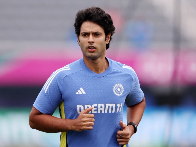 Shivam Dube wearing a blue cricket jersey with yellow accents and the Dream11 logo. The jersey features the Indian cricket team emblem on the chest. He is running on a field, with a blurred background of colorful stands.