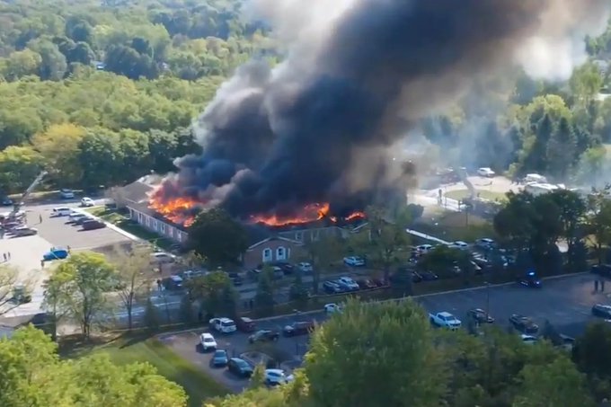 A man in camouflage clothing holding a dead duck, standing by a lake with reeds and water in the background. A second image shows a building on fire, emitting thick black smoke, surrounded by trees, parked cars, and emergency vehicles.