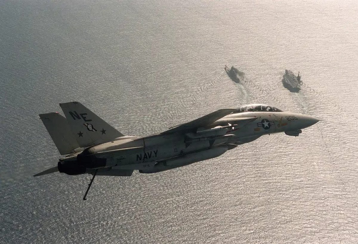 F-14A Tomcat of VF-2 “Bounty Hunters” banks toward USS Ranger (CV-61) during operations in mid-1987. On her port side an Iowa-class battleship. 
This pairing of carriers and battleships was rare in the late Cold War, as Navy briefly reactivated Iowa-class for surface fire support