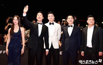 Jung Soojung in a sparkling navy blue sleeveless gown, standing on a red carpet with four men in formal attire. One man in a black tuxedo with a bow tie waves, another in a white tuxedo with a bow tie stands beside him, and two others in dark suits also wave. A "BIFF" banner and photographers are visible in the background.