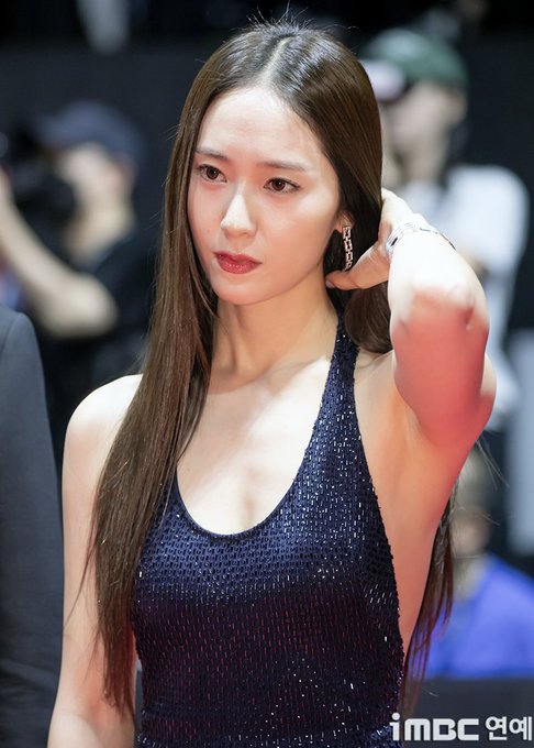 Park Shin-hye wearing a sleeveless, dark blue sequined dress with a halter neckline and side cutouts. Her long, straight brown hair falls over her shoulders. She has dangling earrings and a bracelet on her wrist. A watermark reading "imoc 오메" is visible in the bottom right corner.