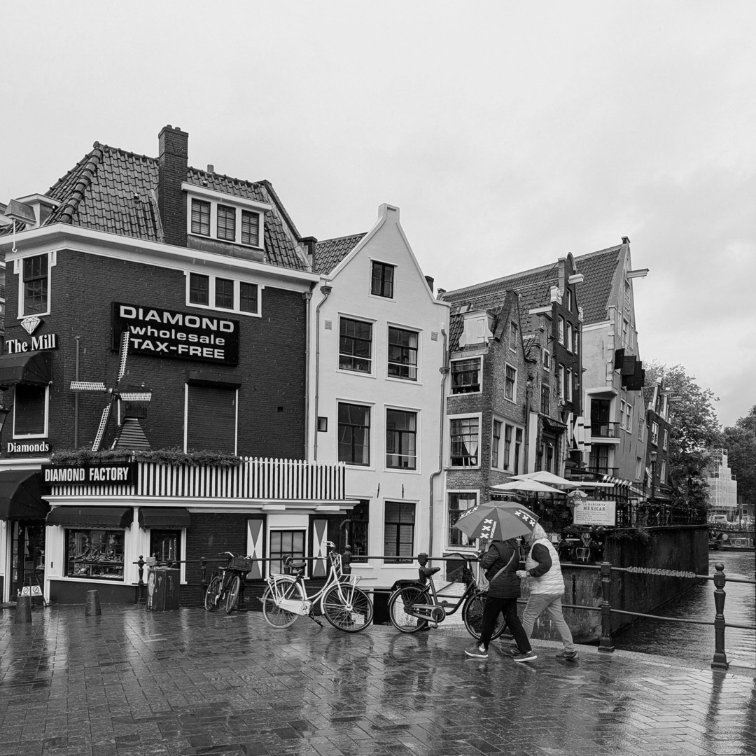 Wet Amsterdam. 

Grimburgwal as seen from Oude Turfmarkt, in downtown Amsterdam. 

And yes, that 'tourist quality' umbrella sports Amsterdam's iconic emblem - a detail of the city's coat of arms.

See our website to learn what those three X's represent. … instagr.am/p/DOtN4ZWCIeZ/