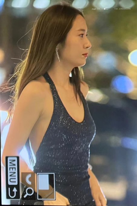 Krystal Jung wearing a sleeveless, black sequined dress with a side cutout, holding a small clutch. Her long, straight brown hair flows over her shoulders. The background features blurred lights and a person in a dark suit, suggesting an evening event. Watermarks from X are visible on the images.