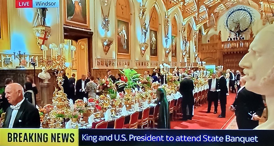 A grand dining hall in Windsor Castle with long tables set for a formal dinner, adorned with flowers and candles, attended by people in formal attire. A bust sculpture and ornate decorations are visible on the walls. A group of children holding containers and bowls, receiving food from adults in an outdoor setting.
