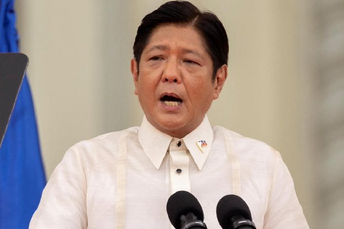 Ferdinand Marcos Jr. stands at a podium, wearing a white barong tagalog with a Philippine flag pin. Two microphones are positioned in front. Benjamin Netanyahu sits at a table, wearing a dark suit, white shirt, blue tie, and a yellow pin. Hebrew text and an emblem are visible in the background.
