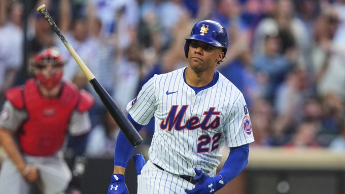Juan Soto vistiendo un uniforme de los Mets de Nueva York con el número 22 en la camiseta. Sostiene un bate de béisbol, de pie en un campo con un receptor en el fondo. La multitud es visible en las gradas.