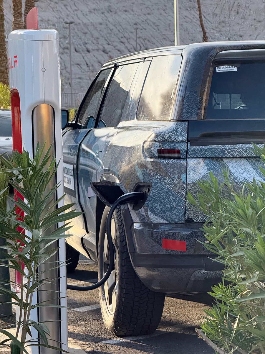 RivianUpdates's tweet photo. Get a look at this Rivian R2 test vehicle charging at a Tesla Supercharger!

Very glad the Rivian R2 is getting native NACS with access to the Tesla Supercharging Network! And the port is in the rear drive side just like Teslas so using V3 Tesla Supercharging stalls will be super easy.

📸: @chrisediting