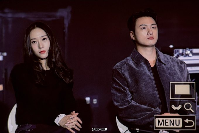 Jung Soojung and Shin Seung Ho standing side by side. Jung Soojung has long dark hair, wearing a black top with white cuffs, hands clasped. Shin Seung Ho wears a dark velvet jacket over a dark shirt, hands in pockets. A watermark "@xxvxxlxt" is visible in the bottom left corner. Text overlays include "MENU" and icons in the bottom right corner.