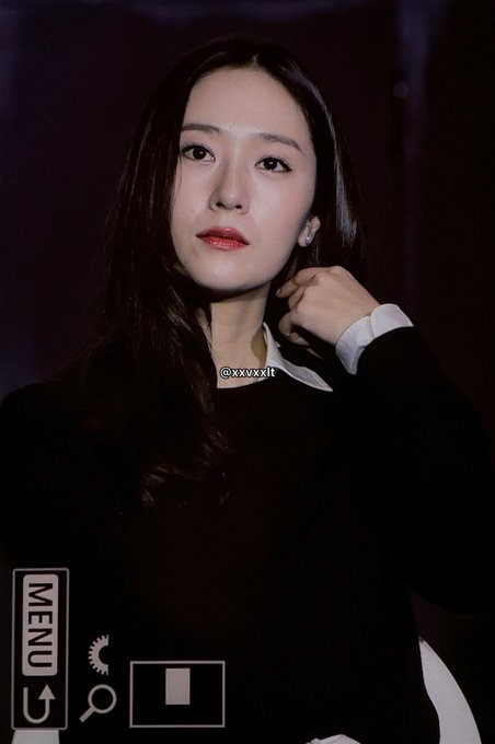 Jung Soojung with long dark hair, wearing a black outfit and white collared shirt. She has a thoughtful expression, touching her chin with one hand. A watermark with "@xxvxxl" is visible.