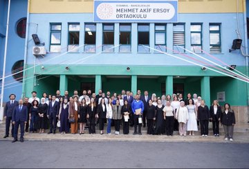 A group of students in yellow uniforms and teachers in formal attire stand in front of Mehmet Akif Ersoy Ortaokulu, a school with a blue and green building. Students reach out enthusiastically toward a man in a blue suit and red tie, Yusuf Tekin, in an outdoor setting with trees and a clear sky. Inside, Yusuf Tekin and others sit at a table, engaging with students and teachers in a room with a mural of Istanbul. Another image shows a large group of students, teachers, and Yusuf Tekin posing together outside the school.