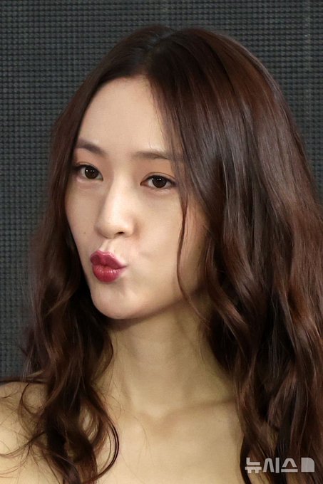 Jung Soojung, also known as Krystal, with long wavy brown hair, wearing a strapless brown top and a wristwatch. She is making a playful expression, puckering her lips in one image and covering her face with her hand in another, showing a ring on her finger. A water bottle is visible in one image, and text in Korean is present at the bottom of the images.