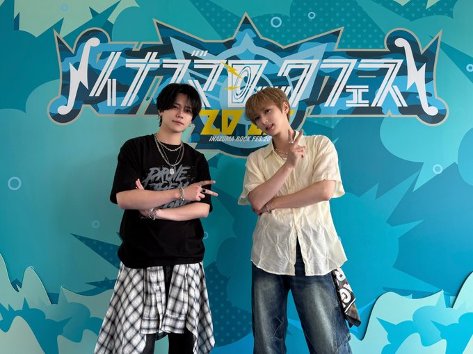 Seven individuals standing in front of a colorful blue background with Japanese text and graphics, including Takumi Ozaki, Kyosuke Fujimaki, and other members of INI. They wear casual outfits like black t-shirts, plaid shirts, and light-colored tops. The text on the background includes "イナズマロックフェス" and "IRF25".