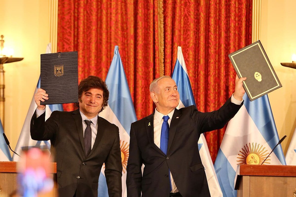 En esta foto con el lamebotas, el genocida sostiene la carpetita de apego argentina al revés. La foto es de la Rosada